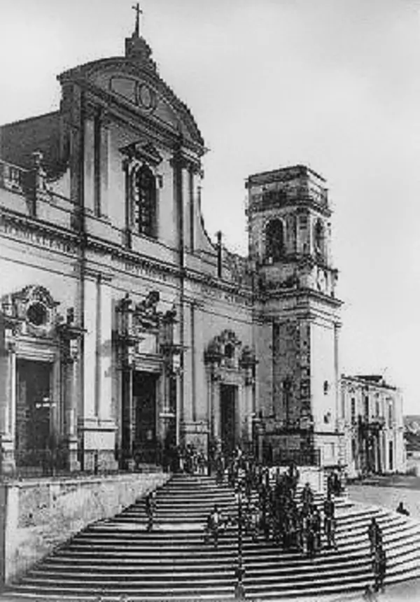 Black and white photograph of the Duomo di Reggio Calabria with a grand Baroque façade, an expansive staircase, and a crowd of people gathered on the steps, highlighting the cathedral’s monumental architecture and historic atmosphere.