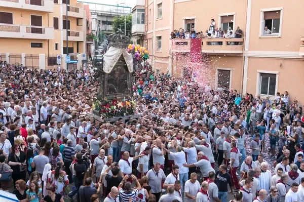 Crowd carrying the richly adorned Vara of the Madonna della Consolazione during the Feast of Our Lady of Consolation in Reggio Calabria, with colorful confetti falling from balconies and spectators lining the street.