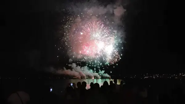 Fireworks illuminate the night sky over the water during the Feast of Our Lady of Consolation in Reggio Calabria, with crowds watching the display near Piazza Duomo.