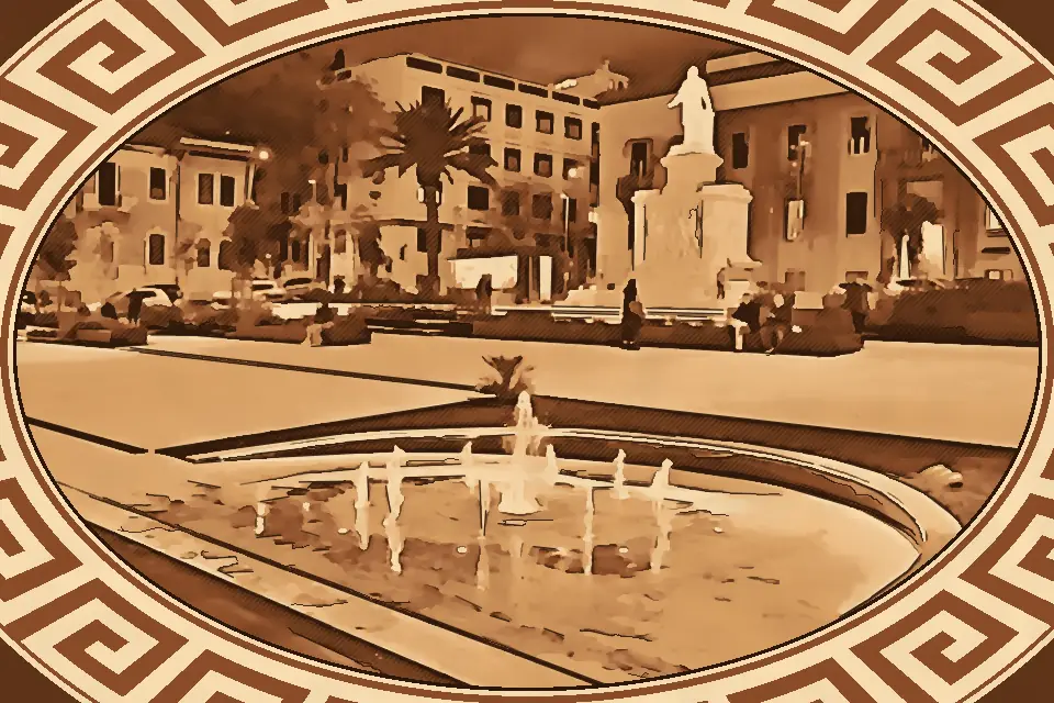 Night view of Piazza De Nava in Reggio Calabria, featuring illuminated fountains, the Monument to Giuseppe De Nava, and surrounding historic buildings, with people relaxing on benches.
