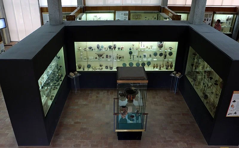 Interior view of the National Archaeological Museum of Locri in Reggio Calabria with illuminated display cases containing ancient Greek and Roman artifacts.